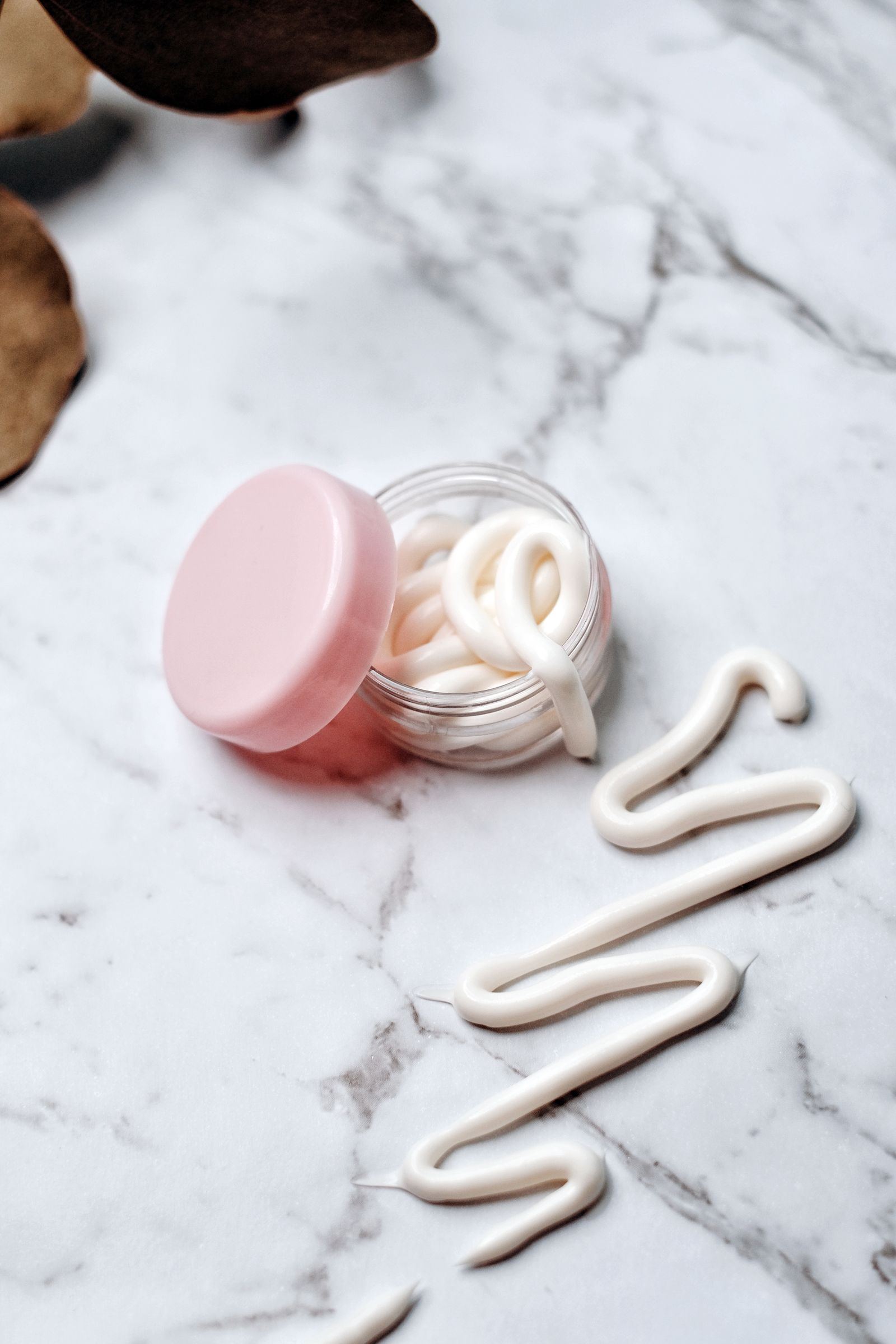 Open skincare cream jar with cream swirled on a marble surface